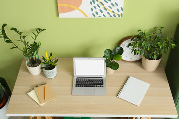 Fototapeta premium Workplace with laptop and green houseplants in office
