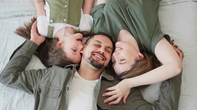 Happy family at home. Mother father children daughter relaxing in bed at home indoor. Mom dad parents kid girl relax playing hugging having fun together. Family smiling laughing enjoying tender moment