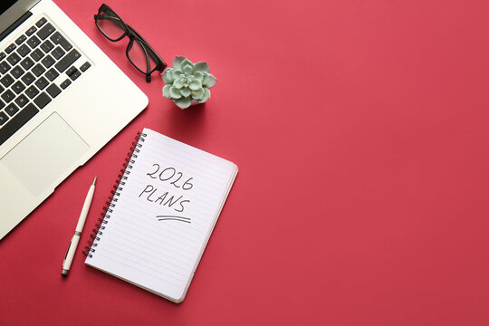 Notebook with text 2026 PLANS, laptop and eyeglasses on red background