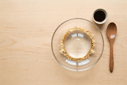 Raindrop cake with kinako powder and brown sugar syrup in a glass bowl on wood table.