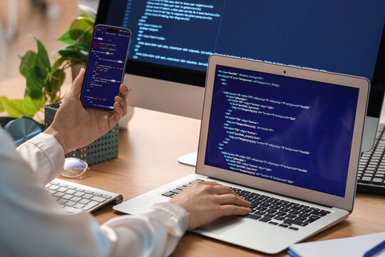 Female programmer's hands working with laptop and mobile phone at table in office, closeup