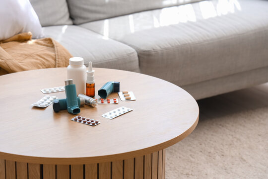 Modern inhalers, pills and medicine on coffee table in living room, closeup
