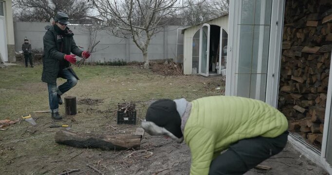 Men with kid cut branches in backyard and stockpile firewood in shed for winter. 4K 10-bit