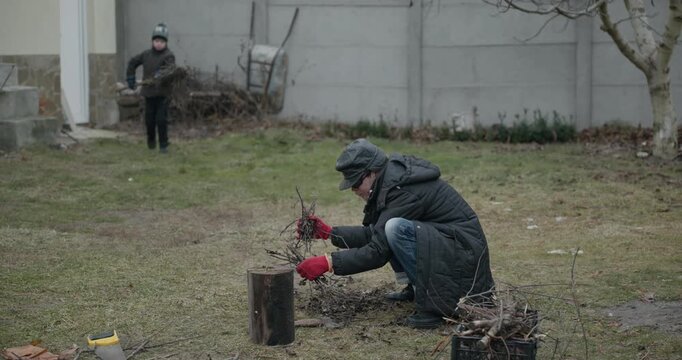 Men with kid cut branches in backyard and stockpile firewood in shed for winter. 4K 10-bit