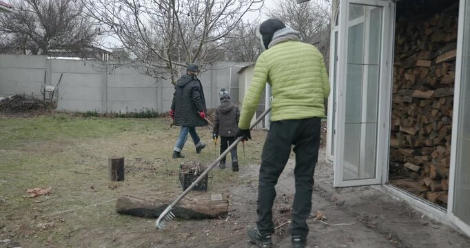 Men with kid cut branches in backyard and stockpile firewood in shed for winter. 4K 10-bit