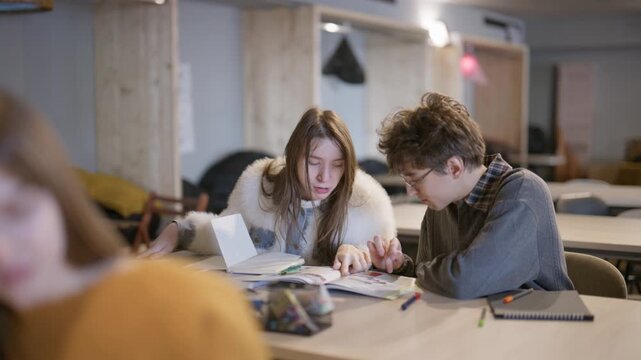 Two young students are focused on a book, discussing their schoolwork together in a bright classroom setting. They are engaged in collaborative learning, sharing ideas and studying side-by-side.