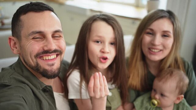 Happy family talk on video call with friends family. Mother father two children daughters talking speaking online at home. Family mom dad parents baby girls kids smiling laughing webcamera view