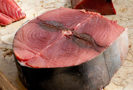 Fresh raw tuna steak with deep red flesh and visible texture displayed on cutting surface at fish market