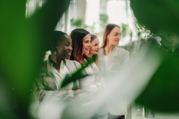 Naklejka premium Diverse group of smiling businesswomen standing together with arms crossed, collaborating in a modern eco friendly office