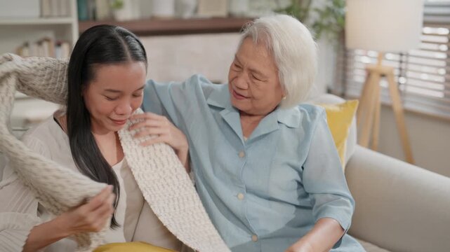 Elderly woman embrace young woman on sofa in home living room, warm family comfort with blanket indoors, elderly woman and adult woman holding knitted blanket, supportive affection and cozy emotion