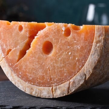 A slice of aged gouda cheese with distinctive holes and a rich orange hue