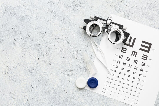 Optical trial frame with eye test chart and set for contact lenses on white grunge background