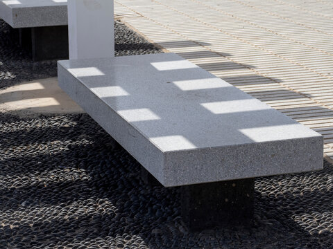 Modern concrete bench casting strong geometric shadows on tiled ground creating abstract light and shadow pattern outdoors