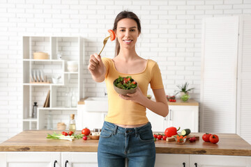 Beautiful young woman with bowl of fresh vegetable salad in kitchen