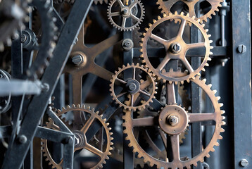Fototapeta premium A complex, aged mechanical clockwork mechanism is displayed. Gears are interlocked and moving, suggesting a timekeeping device. It appears to be housed within an industrial or workshop setting.