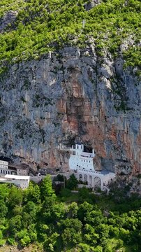 Vertical aerial drone view of Ostrog Monastery in Montenegro. Orthodox Christian monastery built into a vertical rock cliff, famous pilgrimage site.	