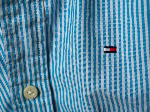 Riga, Latvia - 15.04.2026: Tommy Hilfiger embroidered logo. Close-up of a blue and white striped cotton shirt featuring a small embroidered logo on the chest and a button detail.