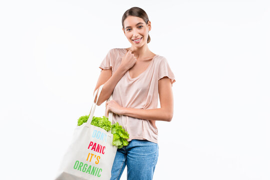 Smiling young woman with reusable grocery bag full of organic products isolated on white background, healthy eating, eco lifestyle, sustainability and natural nutrition concept