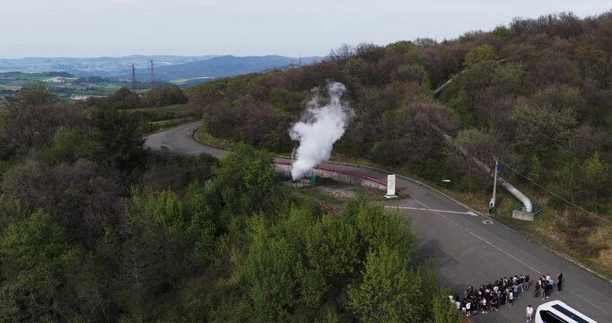 Larderello, Italy - 15 April 2026: Aerial view of the Enel Green Power - Centrale Geotermica di Larderello with a steam vent and tourists by a bus in the Tuscan hills.
