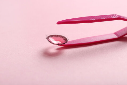 Tweezers with contact lens on pink background