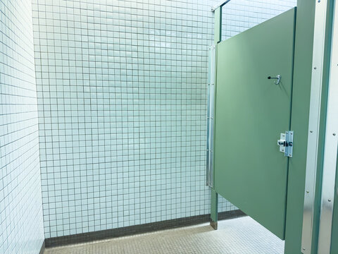 Bathroom stall with green door and tiled walls in public restroom during daytime