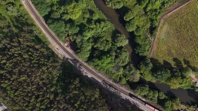 Aerial view of a train cutting through lush greenery alongside a winding river, contrasting with the textures of the landscape, Porto, Portugal.