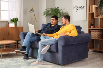 Obraz premium Handsome young brothers sitting on sofa with laptop in living room