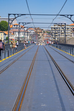 View of the Dom Luis I Bridge with its intricate metalwork casting shadows on the walkway, as pedestrians stroll across it, Porto, Porto District, Portugal.