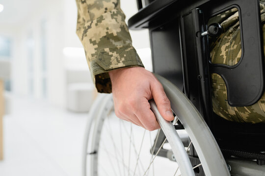 Close up of unrecognizable man in military uniform sitting in wheelchair in hospital corridor, focus on hand gripping wheel rim, rehabilitation, recovery, medical care and healthcare support