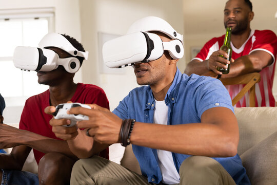 African American men playing VR games in living room with white headsets, controllers, blue shirt