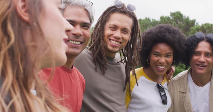 Diverse friends leaning in, laughing together at park as speaker at left telling joke, sunglasses
