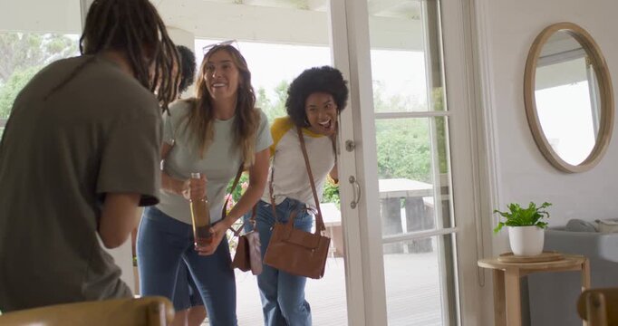 Diverse friends arriving at glass sliding door, handing bottles and hugging host for social visit