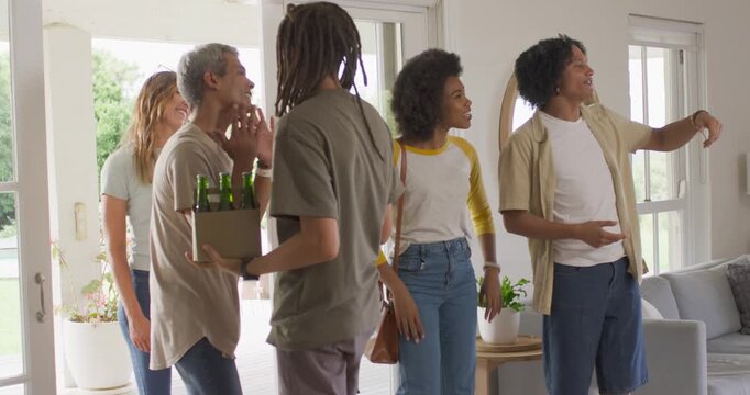 Diverse friends entering as sliding doors open, bringing bottles and hugging host to visit at home