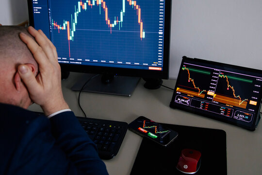 Stressfull trader holding smartphone, using trading app with stock market charts for financial analysis and monitoring investment data.