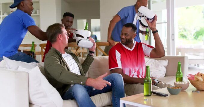 Diverse men on sofa reacting to beer-carrying friend passing VR sets while using gamepad for game