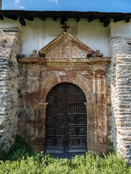 Old wooden door in a cross arch surrounded by carved stone and a cross at the top belonging to the parish church of San Juan de Paluezas - Our Lady of the Assumption