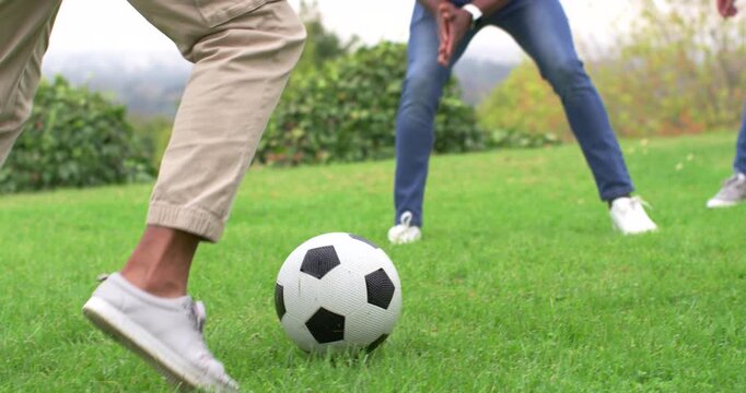 Diverse men, man in khakis, foot-nudging and dribbling soccer ball, keeping ball on lawn