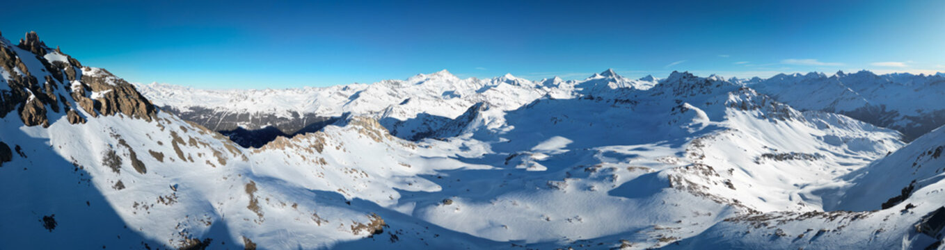 Aerial view of the snow-dusted Becs de Bosson peak under a crisp blue sky, a panorama of stark beauty and jagged rock formations, Anniviers, Valais, Switzerland.