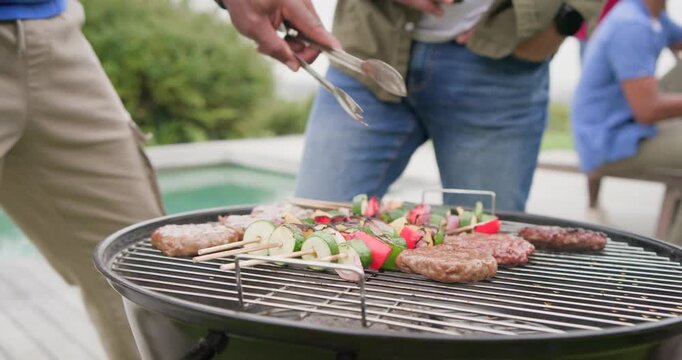 Diverse men watching man spotting patties, holding tongs pressing, flipping kebabs on grill by pool