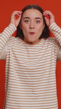 Excited amazed pretty woman in pullover touching head and showing explosion, looking worried and shocked, professional burnout. Looking surprised wow girl isolated alone on red studio wall background