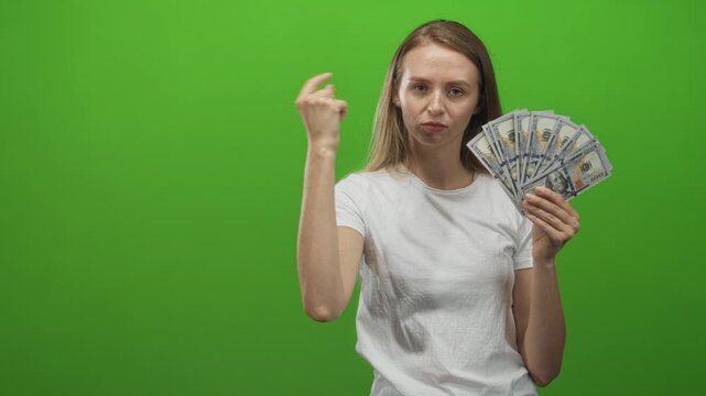 Woman pinches nose holding a fan of dollar bills in studio, also pointing and flicking fingers in sequence; disgust aversion.