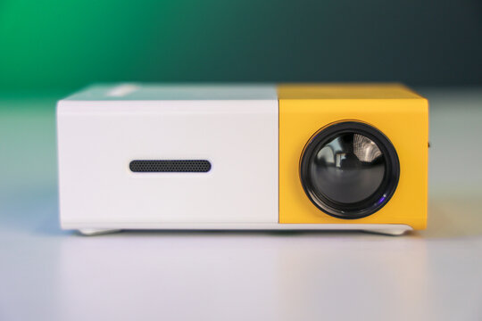 A Small Yellow color mini projector on white table in a Green background