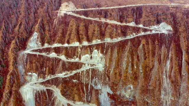 Drone footage of mountain road with serpentine roads, colorful rock and sparse forest landscapes