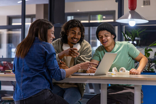 Diverse students leaning in, discussing group project at study lounge with laptop and headphones