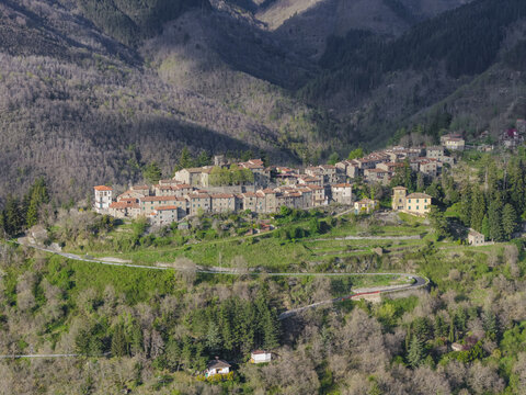 Aerial view of a historic stone village nestled on a lush green hillside surrounded by dense forests and the Apennine Mountains Trappola, Tuscany, Italy.