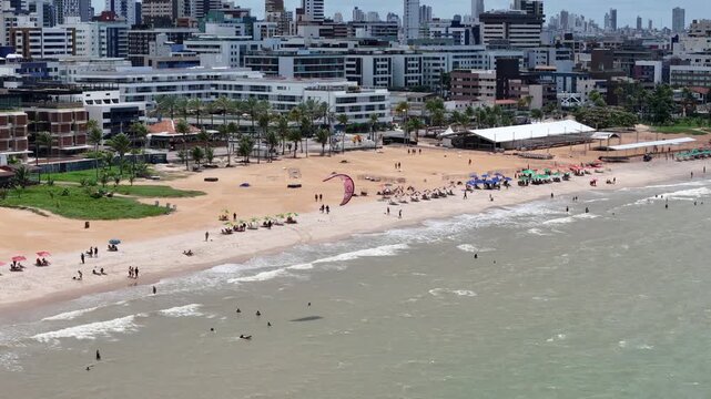 Pessoa praticando kitesurf com v&aacute;rias pessoas na praia e vista panor&acirc;mica do mar em Jo&atilde;o Pessoa, Brasil