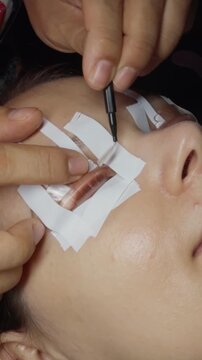 Professional esthetician performing a close up lash lift, applying perming solution to natural eyelashes secured on a silicone rod for enhanced curl, definition, and glamour