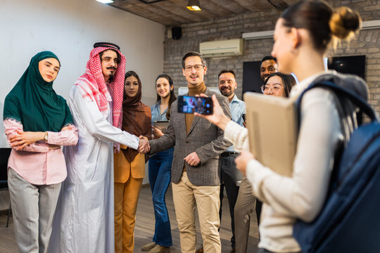 Successful Middle Eastern entrepreneur in traditional thawb shaking hands with diverse business partners in a modern office. Concept of global cooperation and deal closing