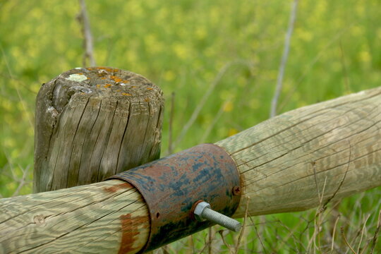 Poste de valla de madera con piezas met&aacute;licas en primer plano, con silueta que recuerda a un p&aacute;jaro imaginario de alas abiertas.