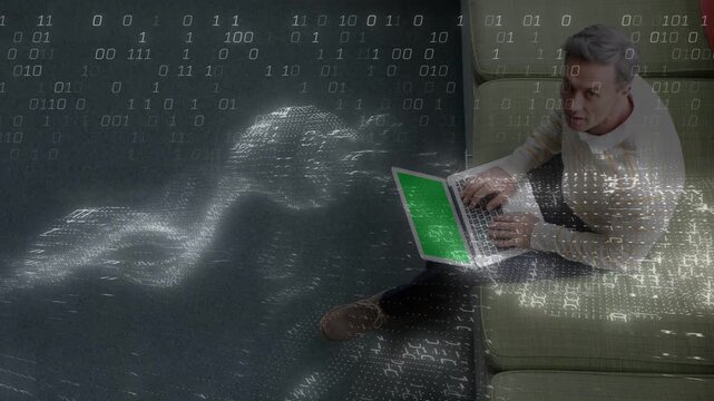 Mature man typing laptop on green sofa, causing binary overlay rippling across dark floor for tech